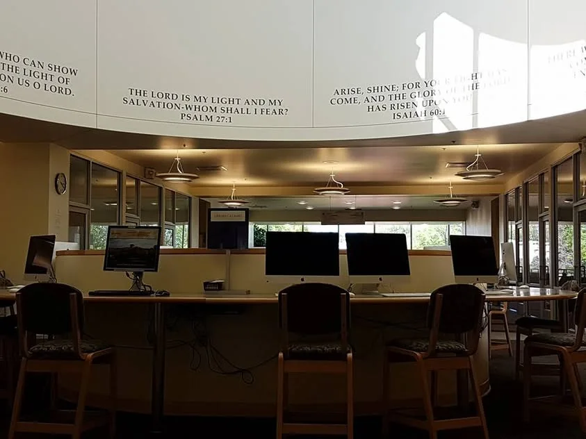 Empty computer workstations sit below Bible verses arranged around a bright upper wall.