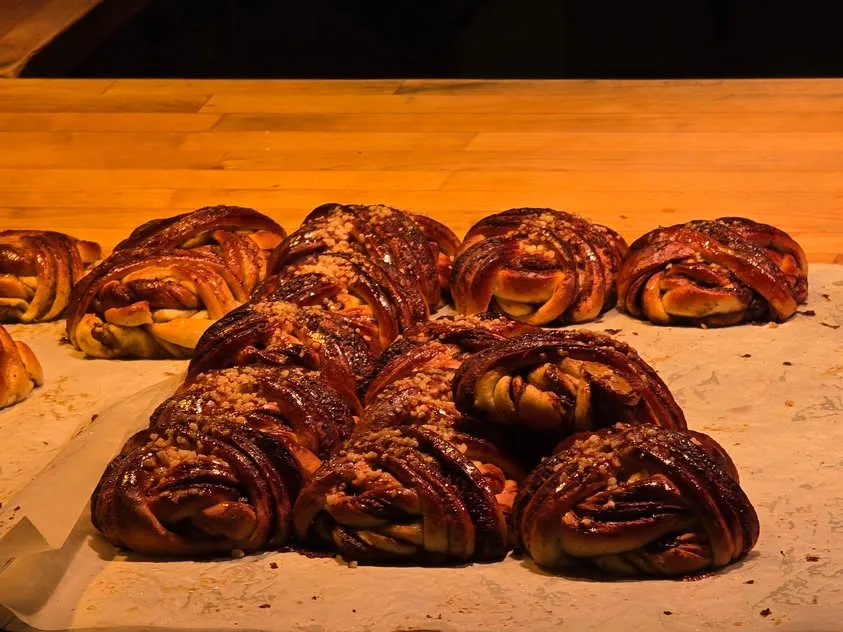 Dark golden knotted pastries sprinkled with sugar sit on a paper-lined bakery tray.