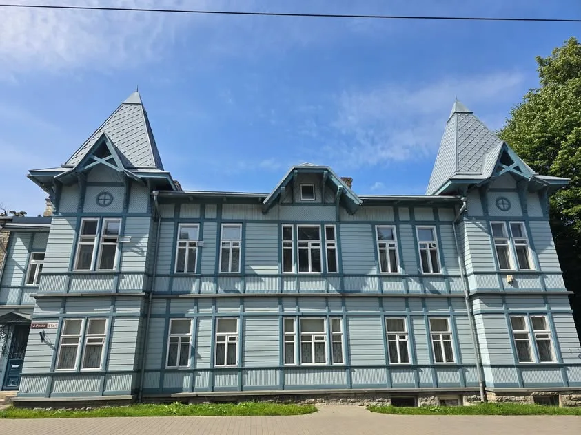 A pale blue wooden building has white-trimmed windows and pointed roof towers.