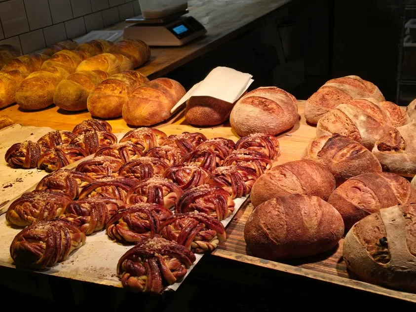 Round loaves and dark golden knotted pastries fill a bakery counter.