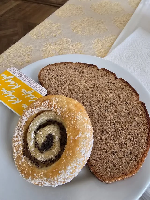 Brown bread and a sugar-dusted spiral pastry sit on a white plate.