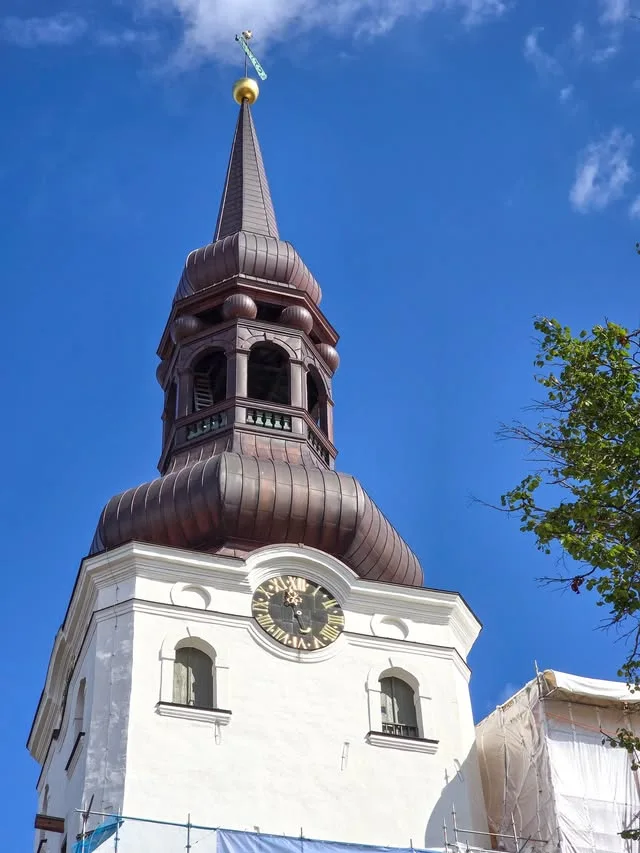 A copper-coloured spire rises above a white clock tower.