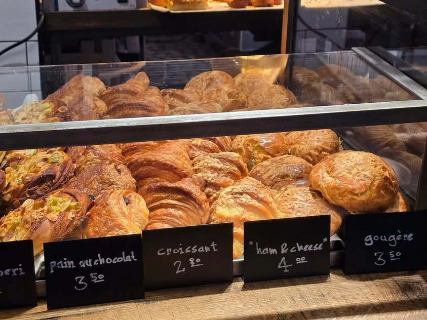 Croissants, chocolate pastries and round baked goods fill a glass display.