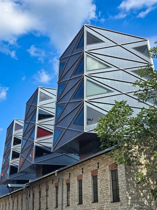 Faceted metal volumes with triangular windows project above an older stone building.