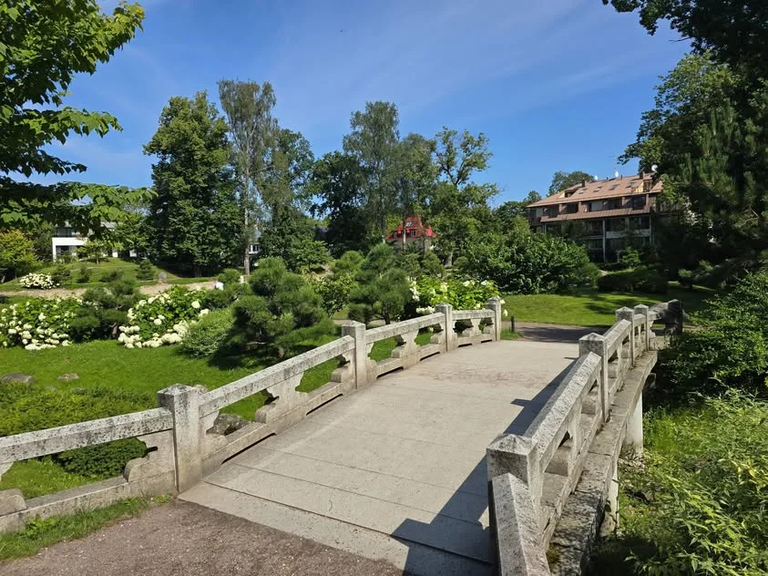 A low stone bridge crosses beside hydrangeas, shrubs and trees.
