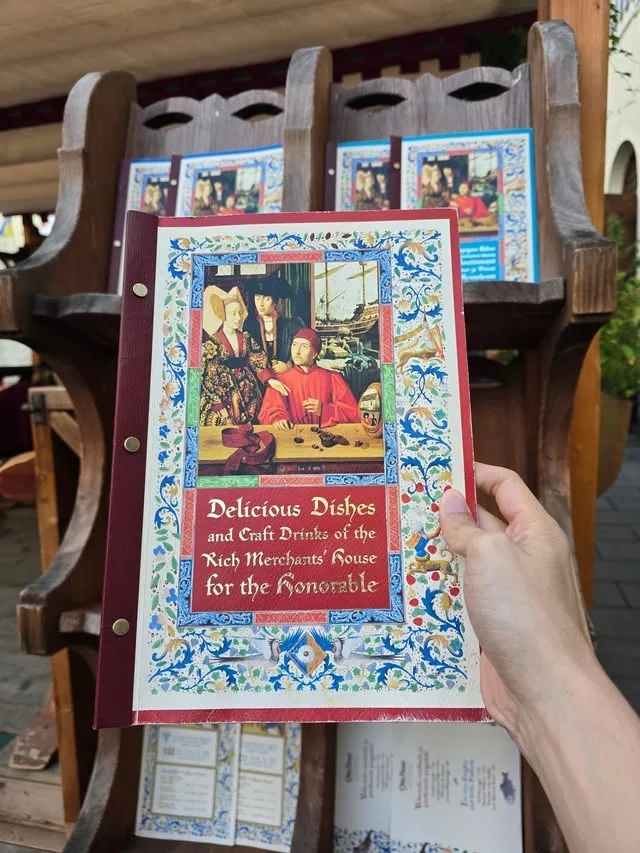 An illustrated merchant-house menu is held in front of wooden chairs.