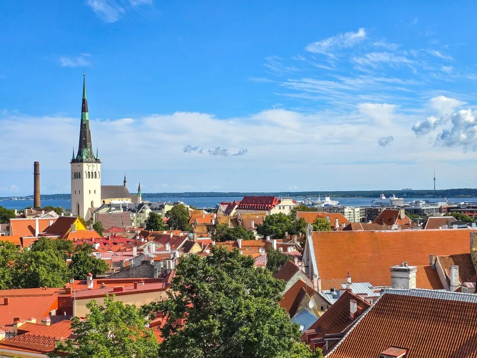 Red and orange rooftops surround a tall church spire, with the harbour and sea beyond.