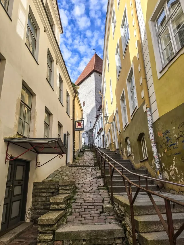 A narrow stone staircase climbs between cream and yellow buildings.