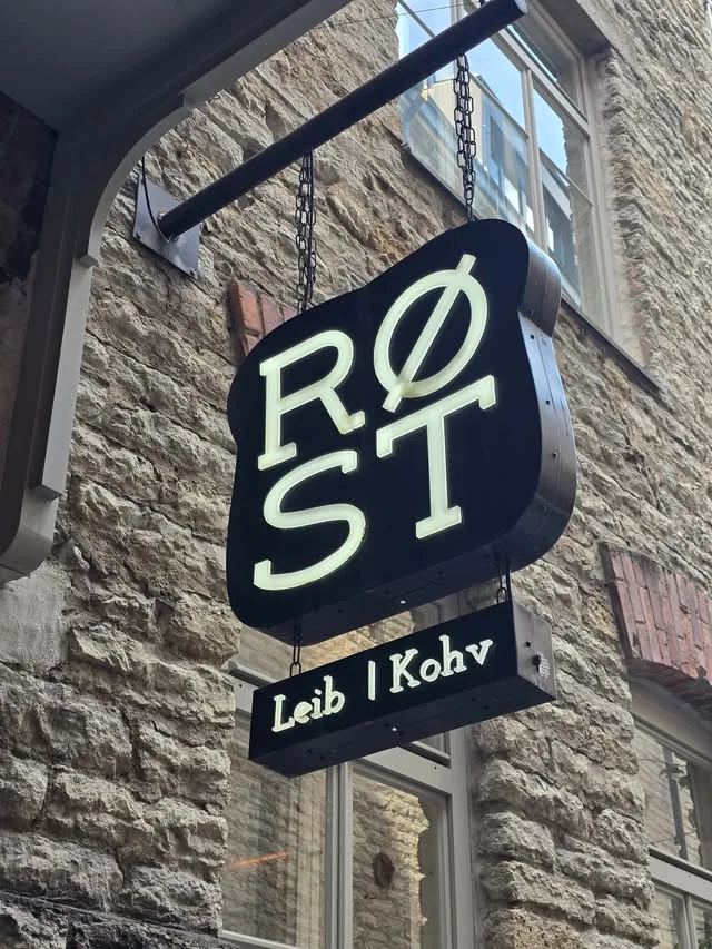 A black illuminated RØST sign hangs from chains against a stone wall, above a smaller Leib | Kohv sign.