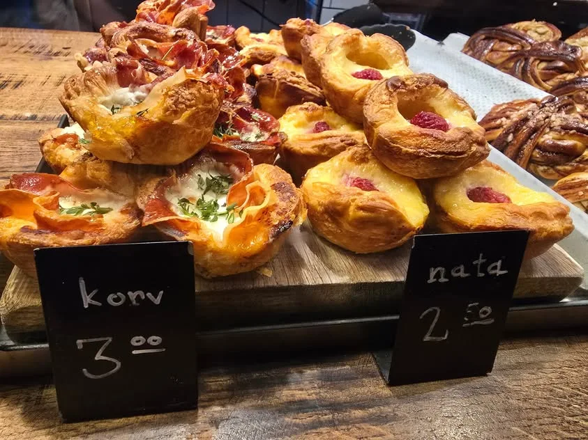 Sausage pastries and custard tarts sit beside chalk labels.