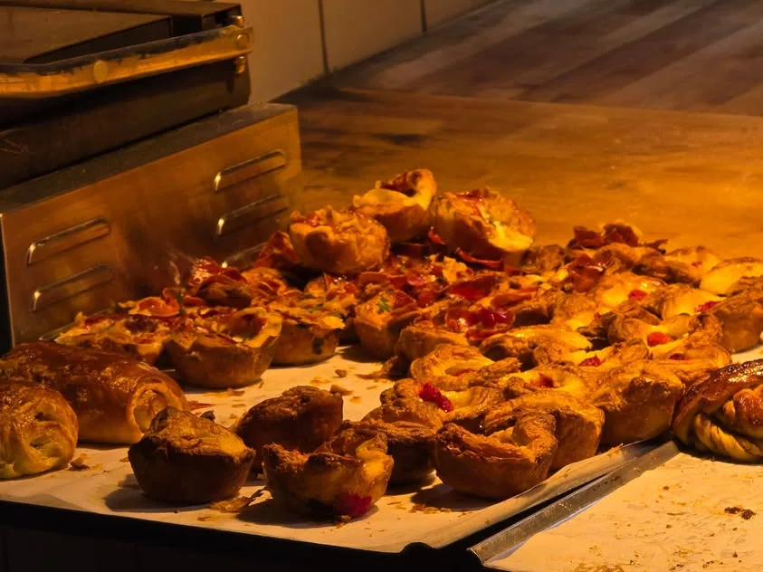 Small savoury pastries sit beneath warm lights on a bakery counter.