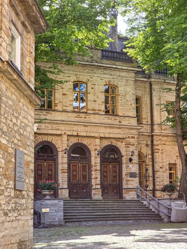 Arched wooden doorways and shallow steps sit beside a shaded stone building.