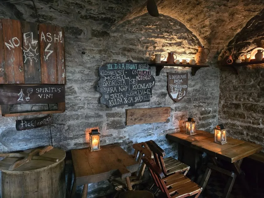 Lanterns light empty wooden tables beneath chalkboards on a stone wall.