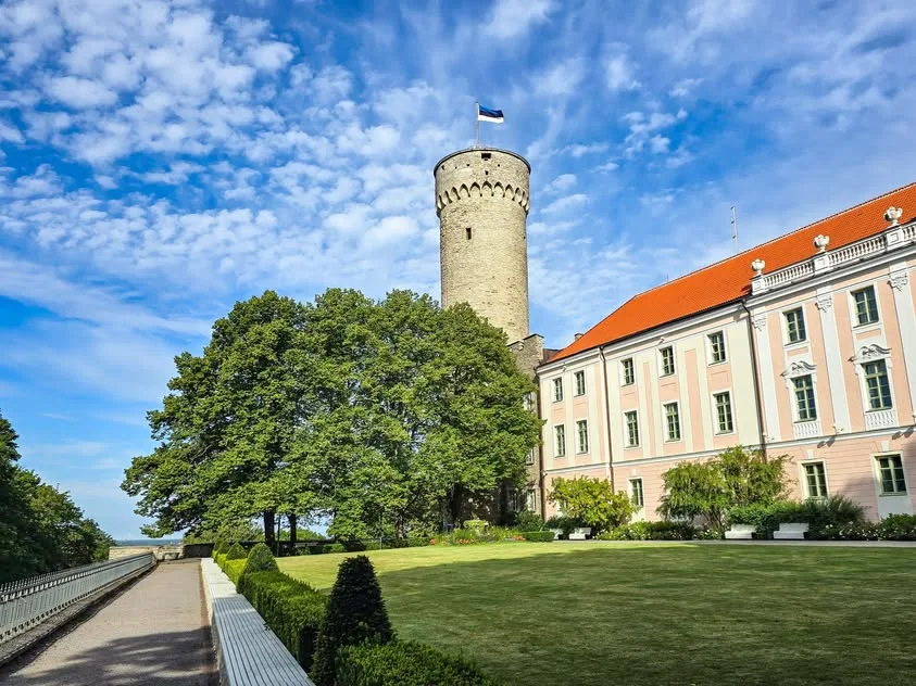 A stone tower stands beside a pink and white building above a manicured lawn.