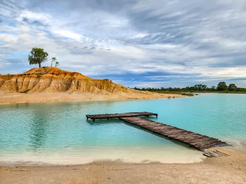 A low wooden jetty reaches into bright turquoise water beneath ochre banks at Blue Lake Bintan.