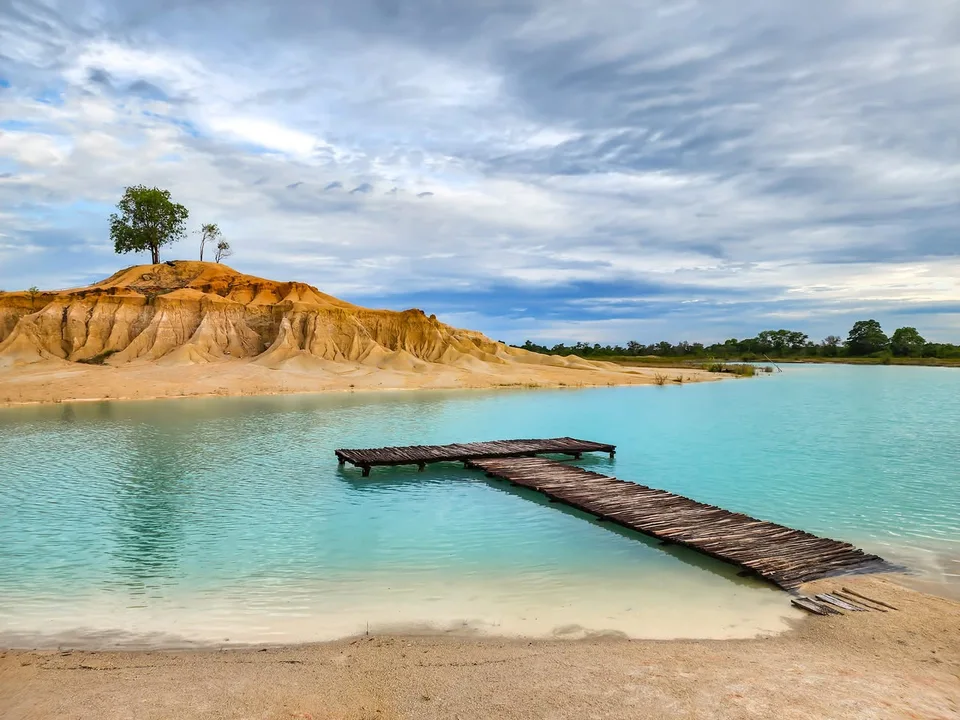 A low wooden jetty reaches into bright turquoise water beneath ochre banks at Blue Lake Bintan.