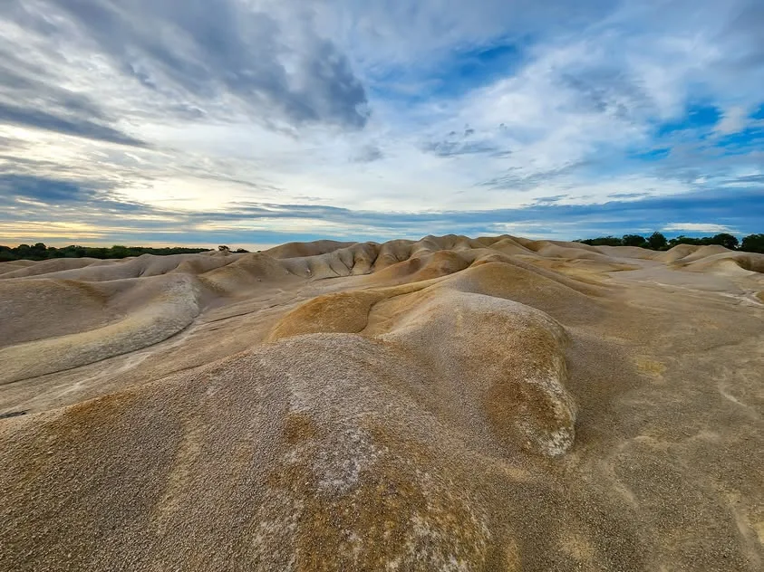 Rounded ridges of pale sandy ground stretch beneath a blue, cloud-filled sky.