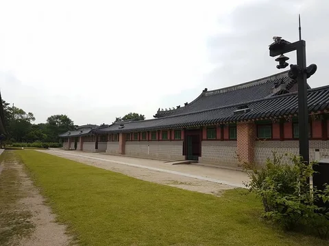 A long palace building with tiled roofs and red-and-green shutters borders a green lawn.