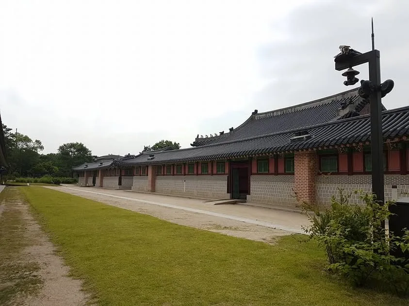 A long palace building with tiled roofs and red-and-green shutters borders a green lawn.