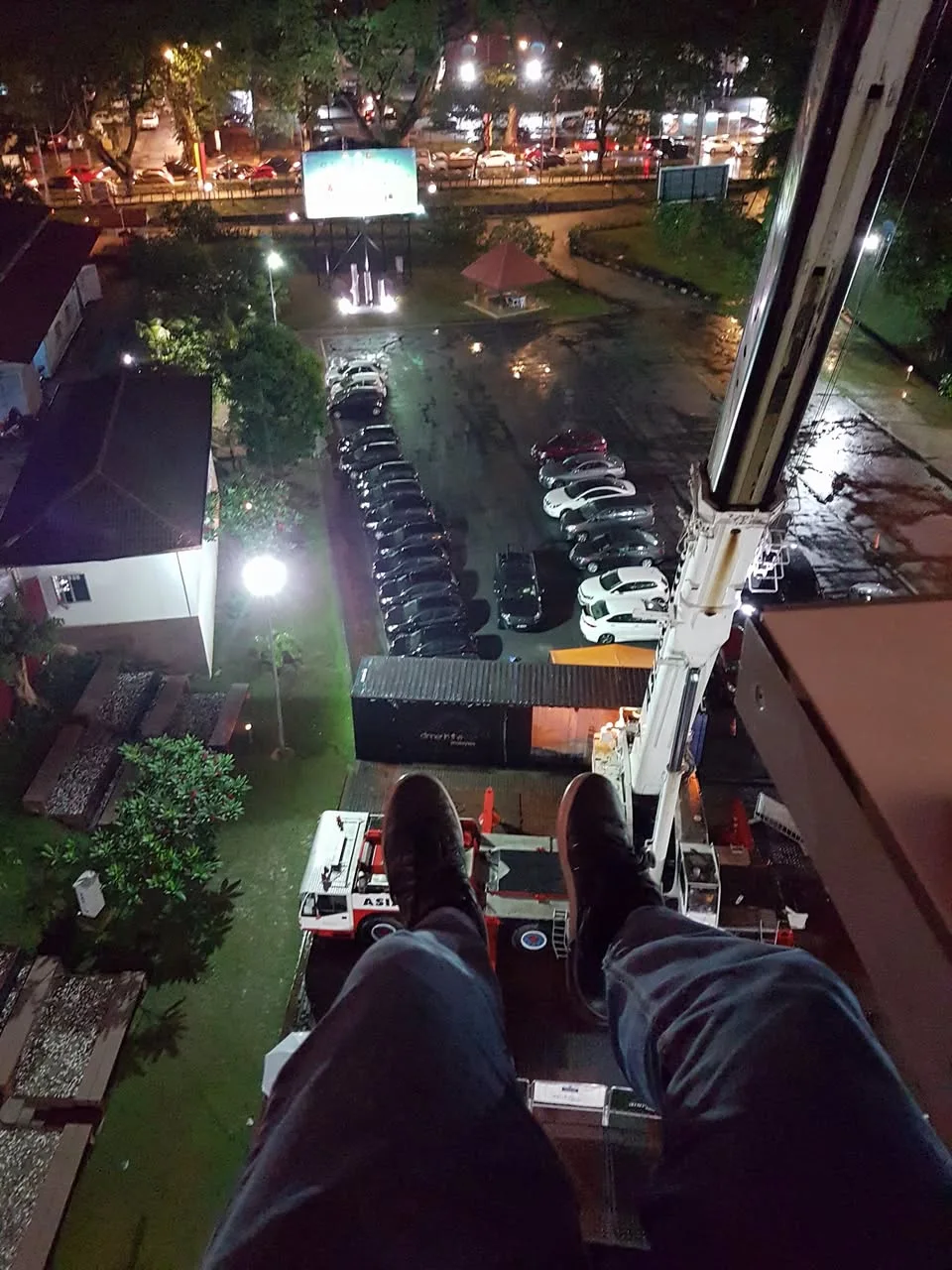 A pair of shoes hangs above a lit car park, with a crane column beside the raised platform.