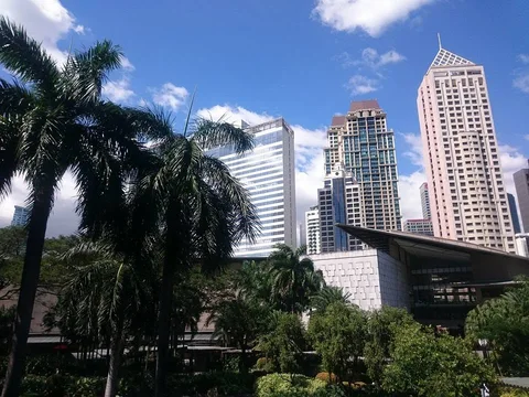 Palm trees and dense garden planting frame the angular Greenbelt building and high-rise towers against a blue sky.