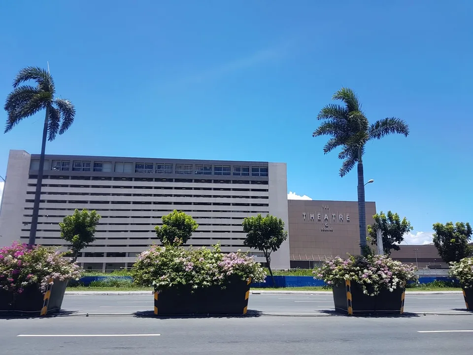 The Theatre at Solaire sign appears on a pale building behind palm trees and roadside flower planters.