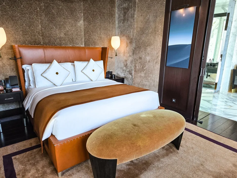 A neatly made bed stands beside tall windows in the Banyan Tree Doha room.
