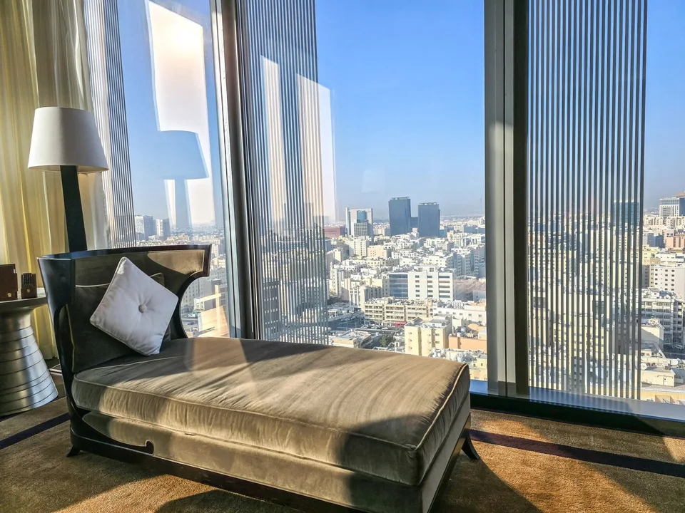 A long chaise sits beside full-height windows overlooking Doha’s buildings.