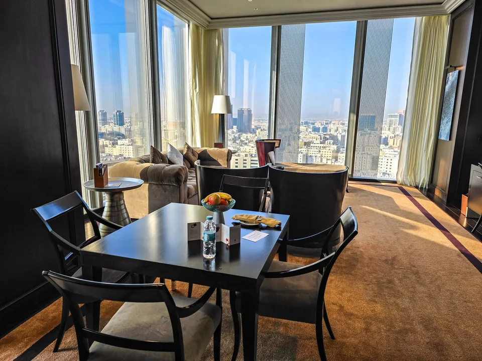 A dining table and armchairs stand beyond the sofa in a spacious hotel sitting room.
