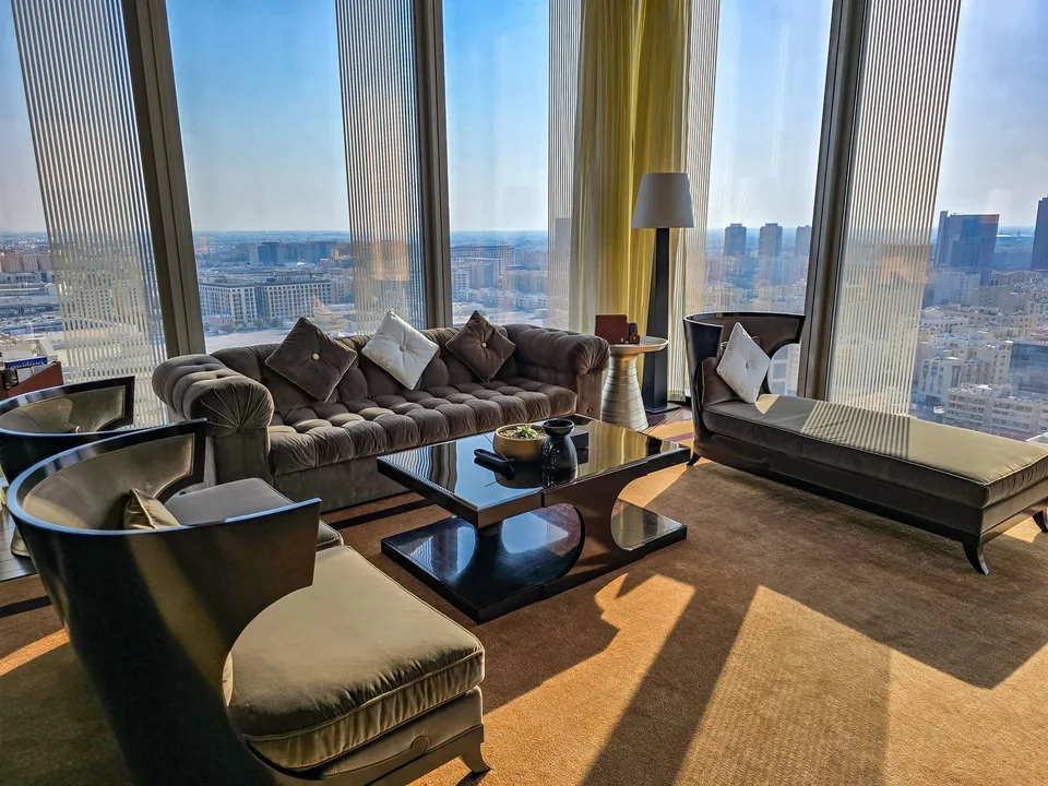 A sofa, chaise and armchairs sit beside full-height windows overlooking Doha.