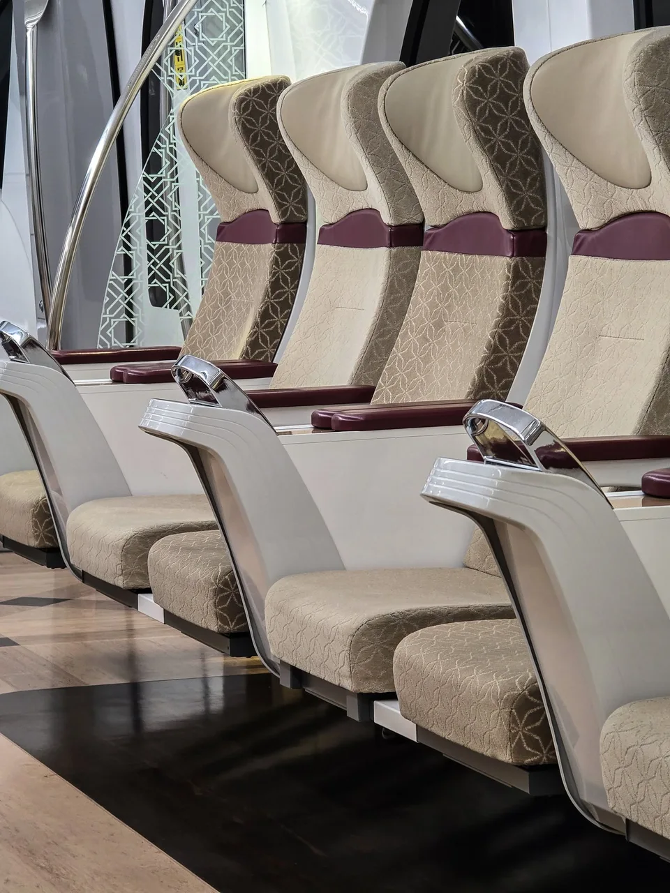 Empty cream-and-burgundy upholstered seats with metal cup holders line a Doha Metro Gold Class cabin.