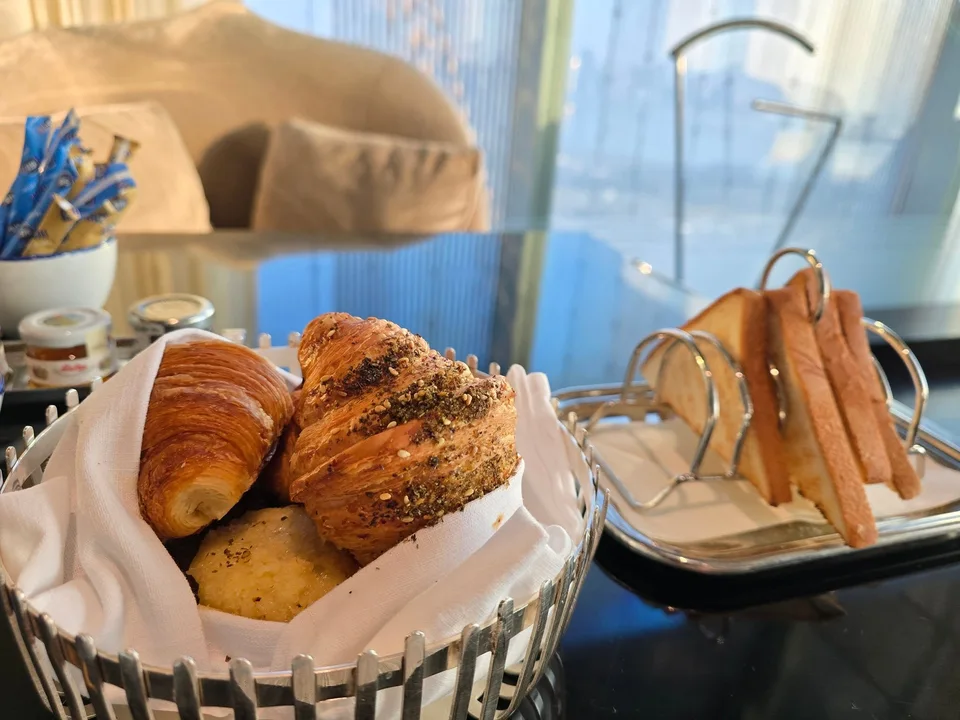 Croissants fill a bread basket beside a rack of toast and small jam jars.