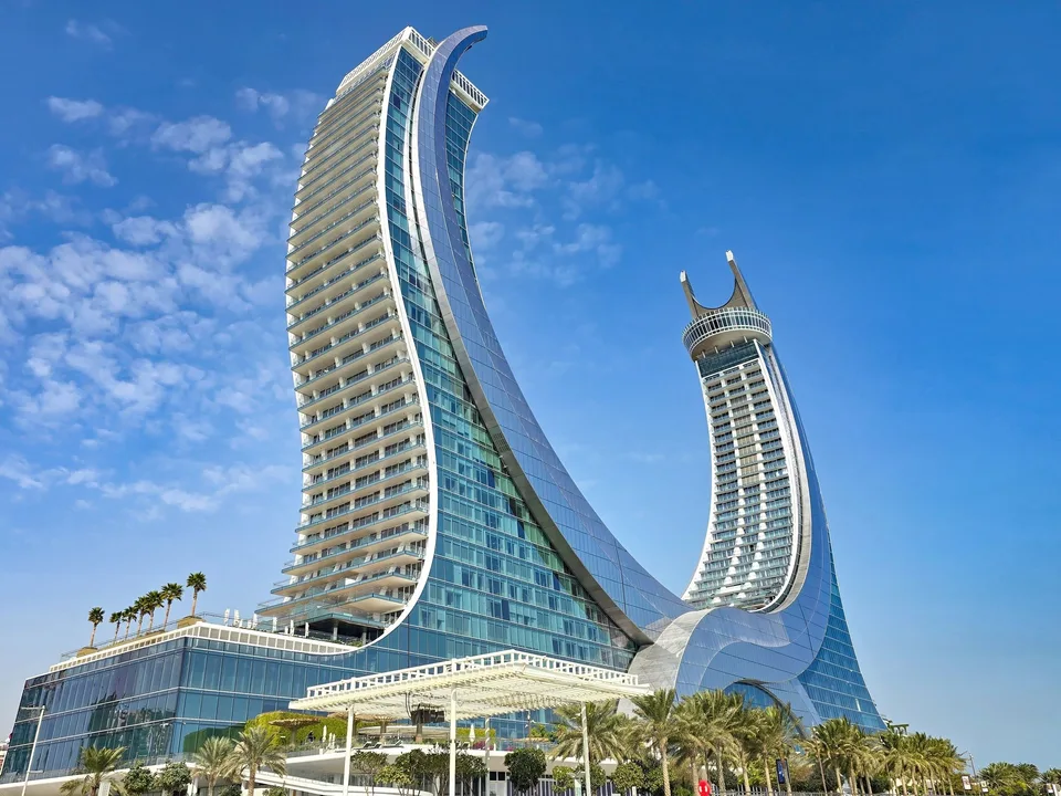 The two curved wings of Katara Towers rise above the Lusail waterfront under a blue sky.