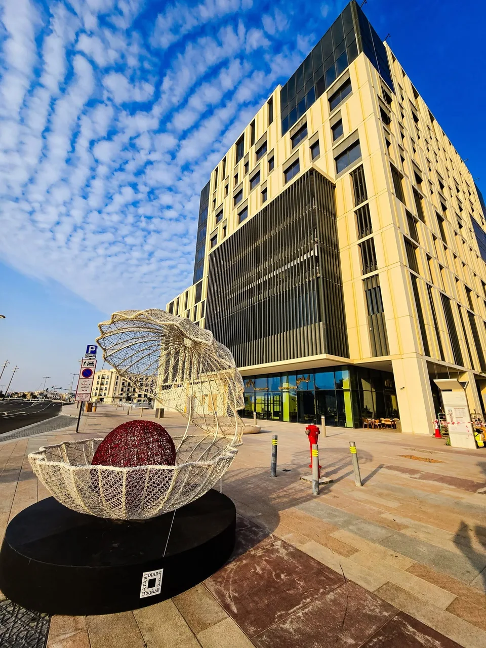 An openwork metal oyster shell holds a spherical pearl beneath the Lusail towers.