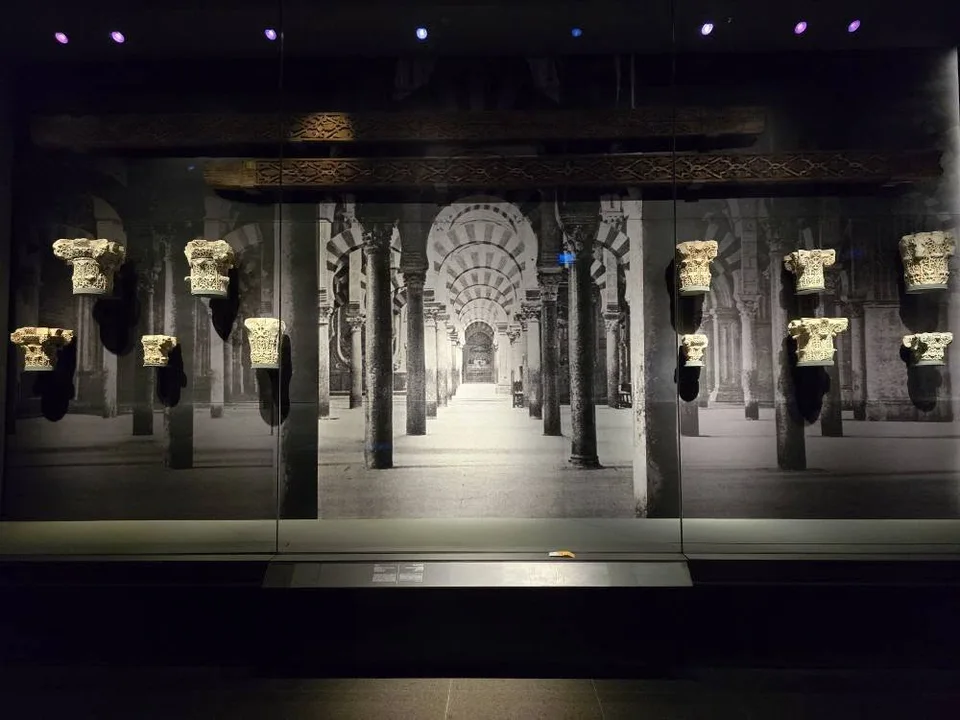 Carved architectural capitals stand before a black-and-white photograph of an arched interior.