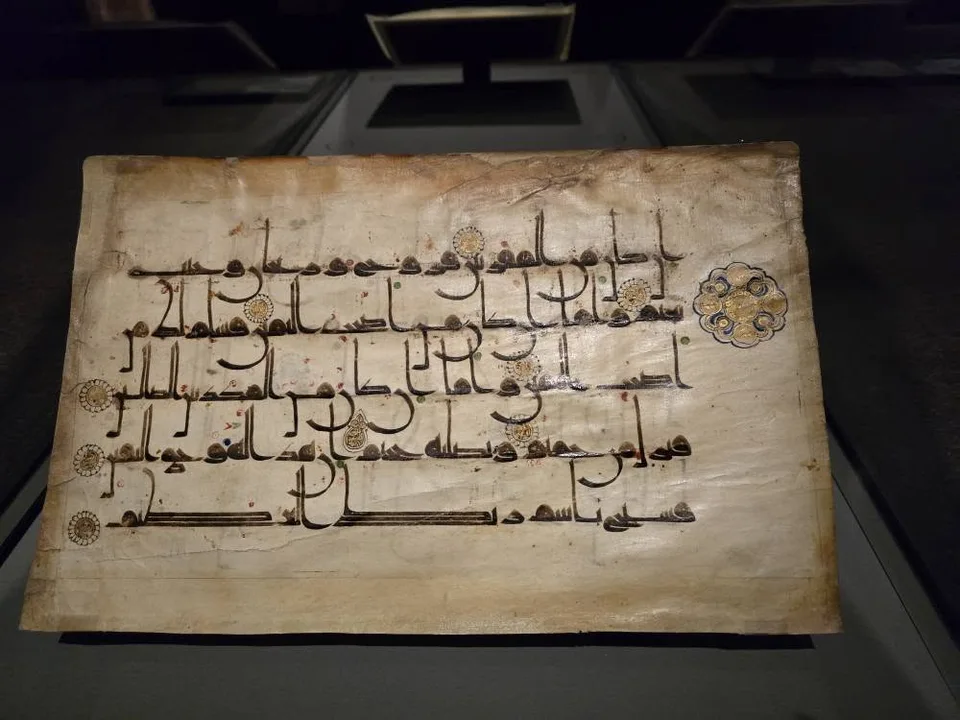 Dark angular Arabic writing and gold roundels cover a single pale manuscript leaf.