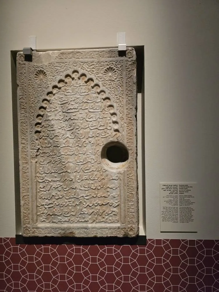 A rectangular pale stone panel bears rows of carved Arabic lettering around an opening.