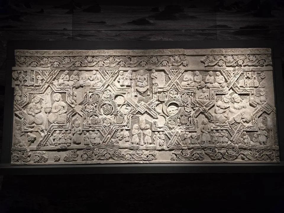 A weathered stone relief contains carved figures and animals in a rectangular composition.
