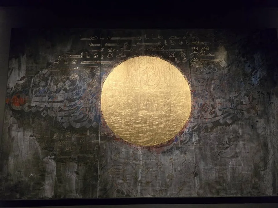 Interlocking gold forms create a large circular calligraphic artwork against a dark wall.
