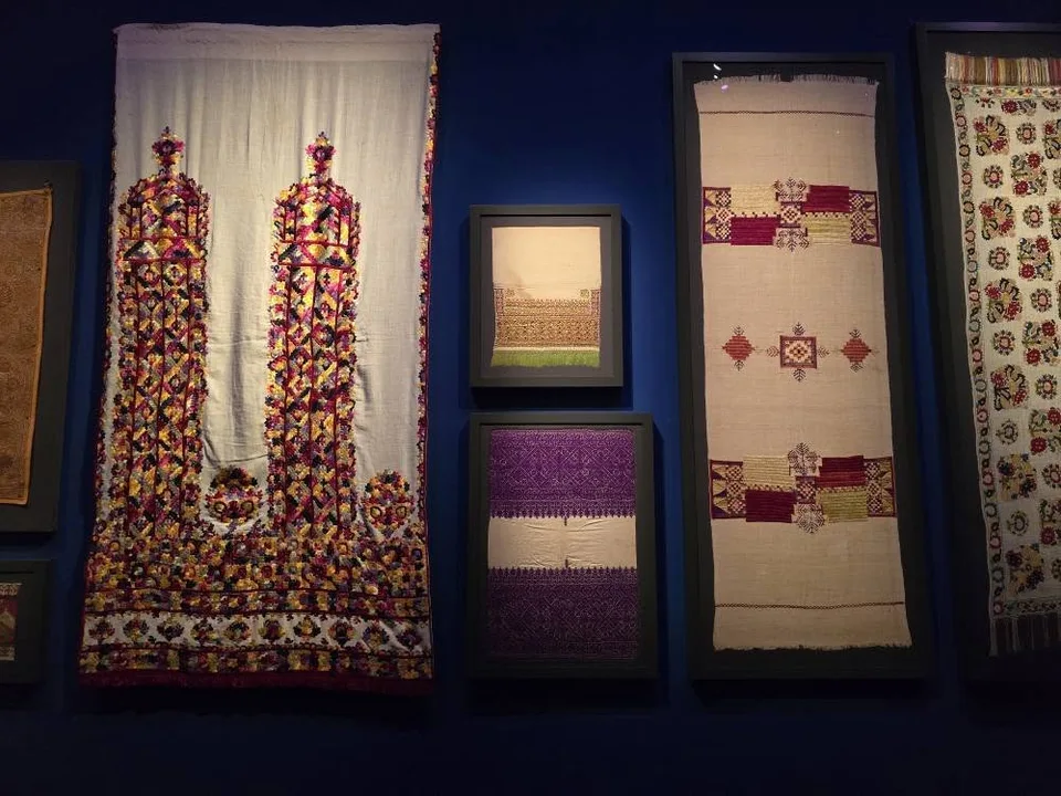 Red, purple and gold embroidered textiles hang vertically in a museum display.