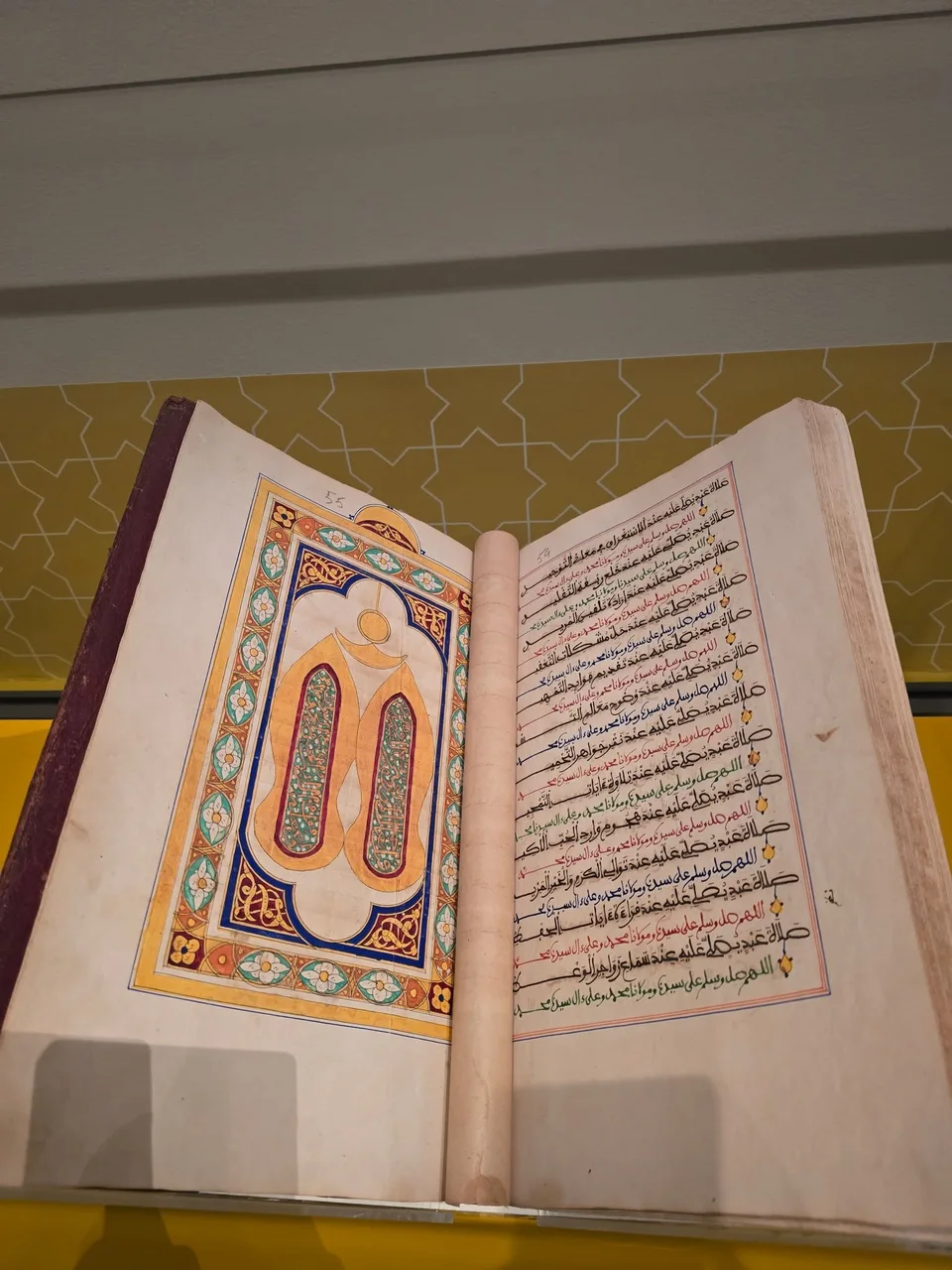 An open manuscript shows two arched illustrations facing lines of multicoloured Arabic calligraphy.