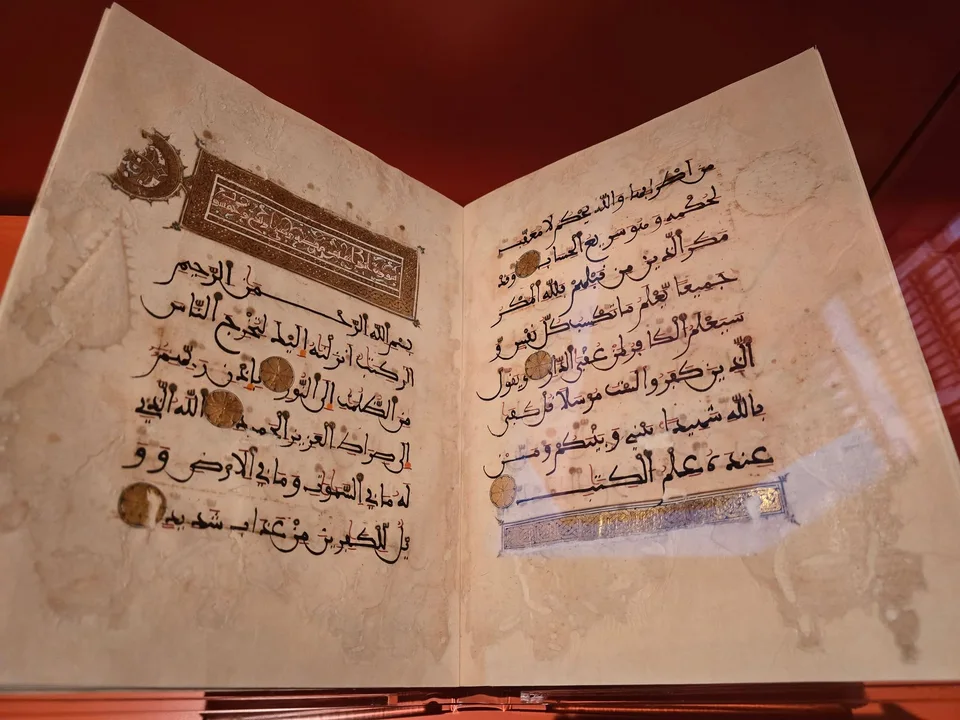 An open manuscript displays Arabic calligraphy and gold ornament on pale pages against a red backdrop.