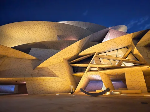 Interlocking discs of the National Museum of Qatar glow gold beneath a deep blue evening sky.