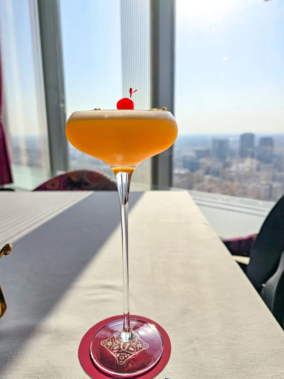 An orange-coloured drink is served in a glass with a small red garnish.