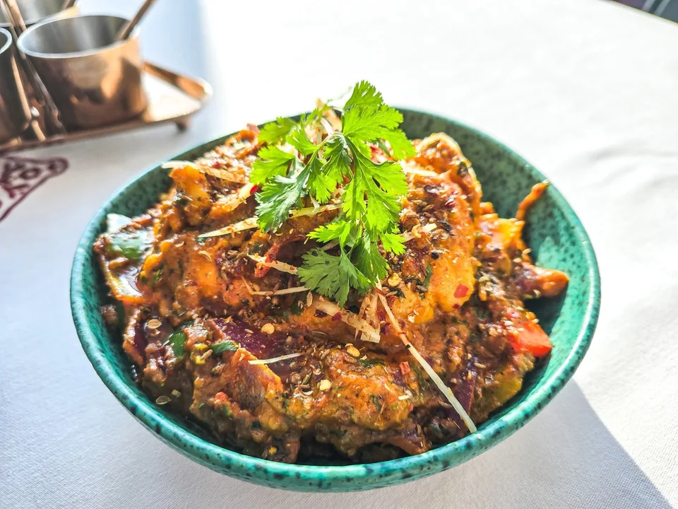 Lobster curry fills a green bowl, topped with fresh herbs and thin strips of ginger.