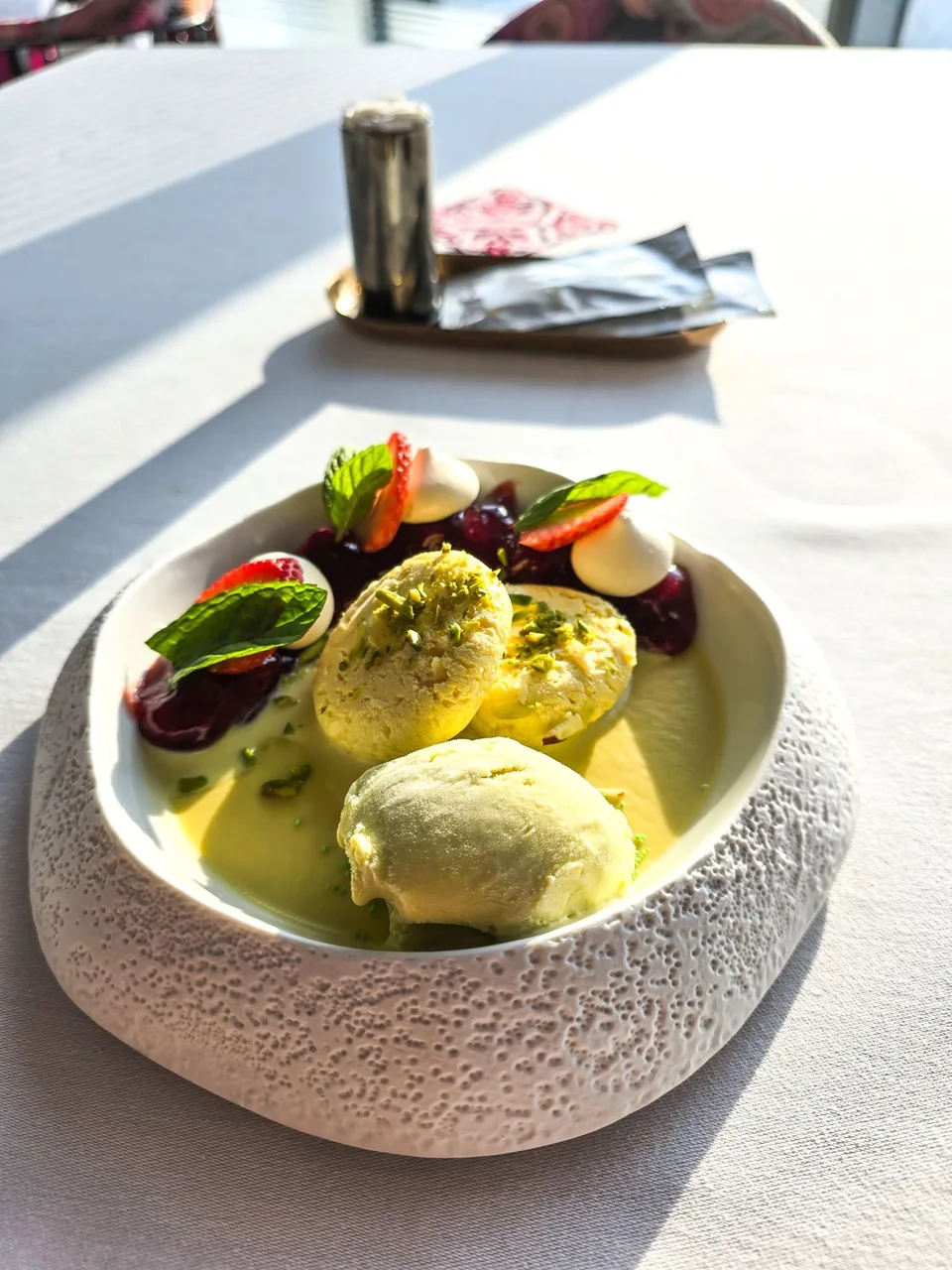 Rasmalai and ice cream are served in a pale textured bowl with strawberries and mint.