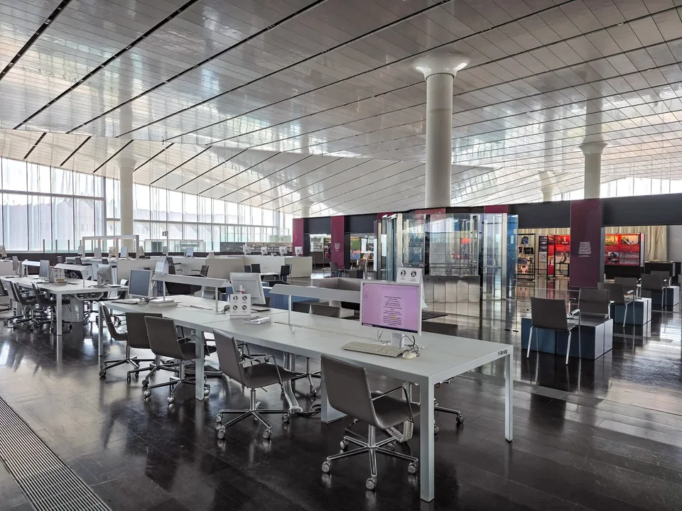 Rows of computer desks stand beneath the high reflective ceiling and tall windows of Qatar National Library.