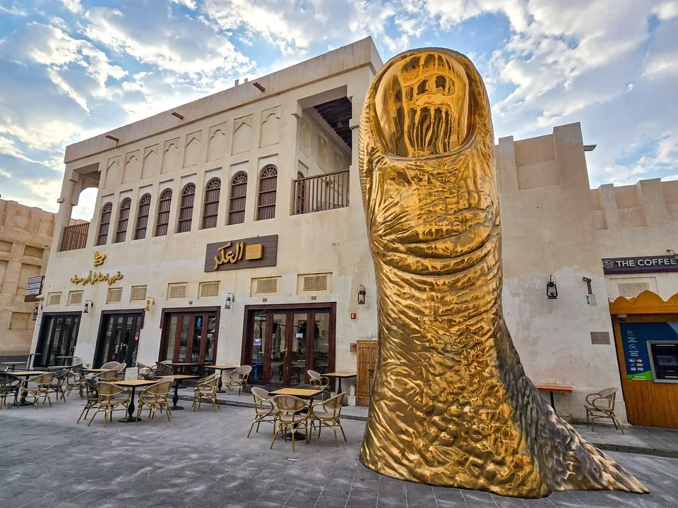A large golden thumb sculpture stands beside outdoor café tables at Souq Waqif.