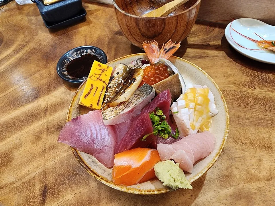 A chirashi bowl is piled with sliced fish, roe, prawn and a yellow piece marked with Japanese characters.
