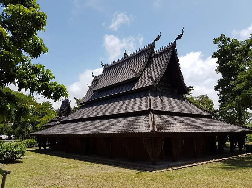 A timber hall with a broad layered roof sits among trees and green planting.